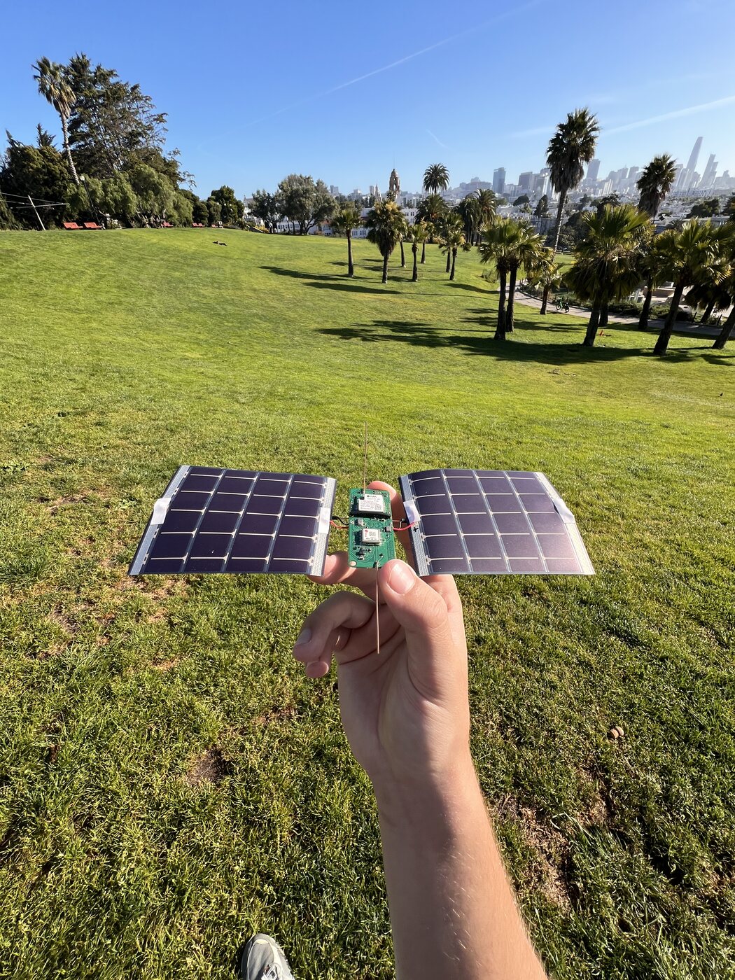 The Stratolink 3 payload held above the grass at Dolores Park, with its two solar panels and wire antennas.
